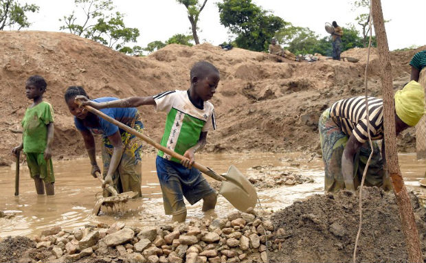 Children working in a muddy area with shovels, gathering rocks and minerals.